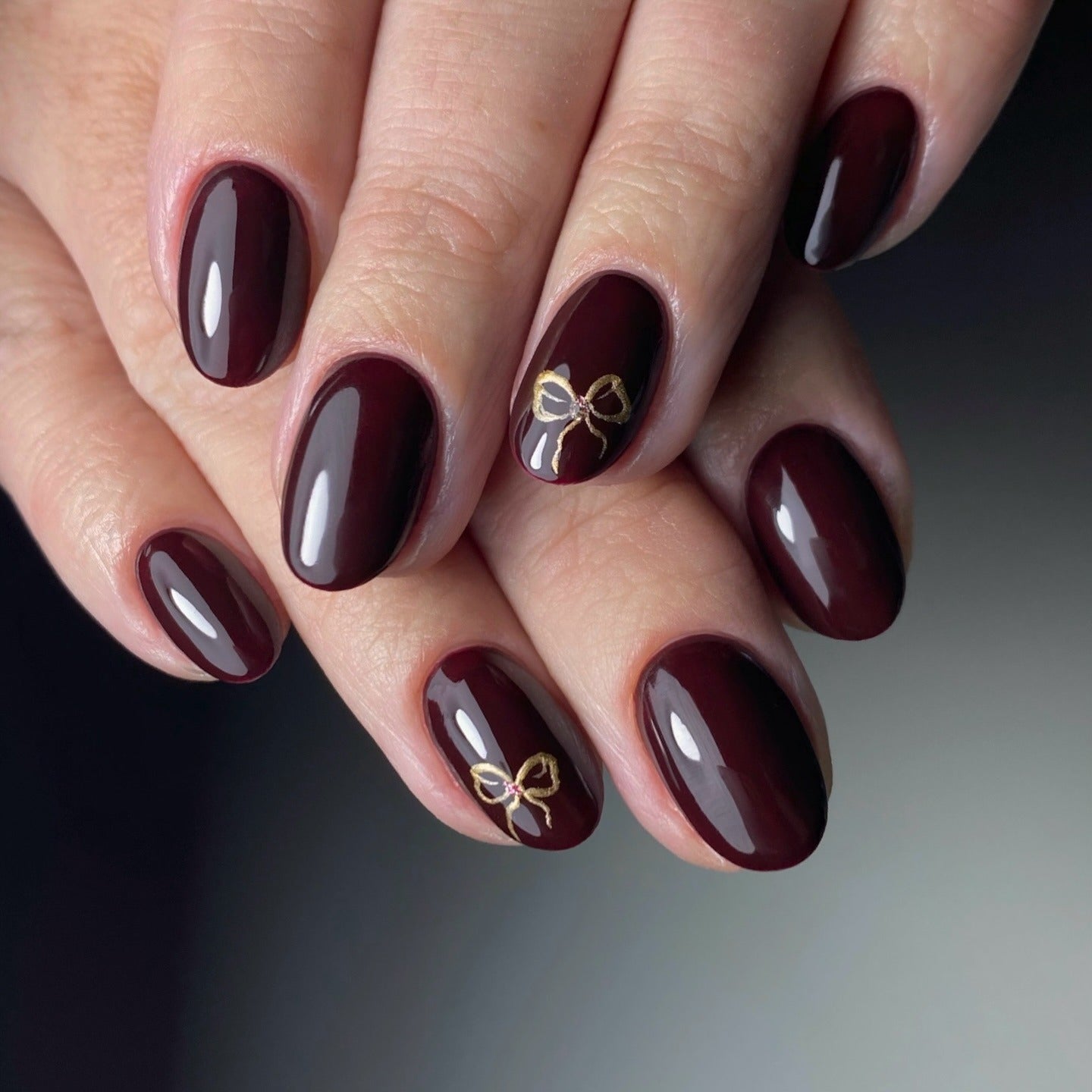 4. Glossy Burgundy with Minimal Gold Bow Detail (Burgundy Nail Ideas)