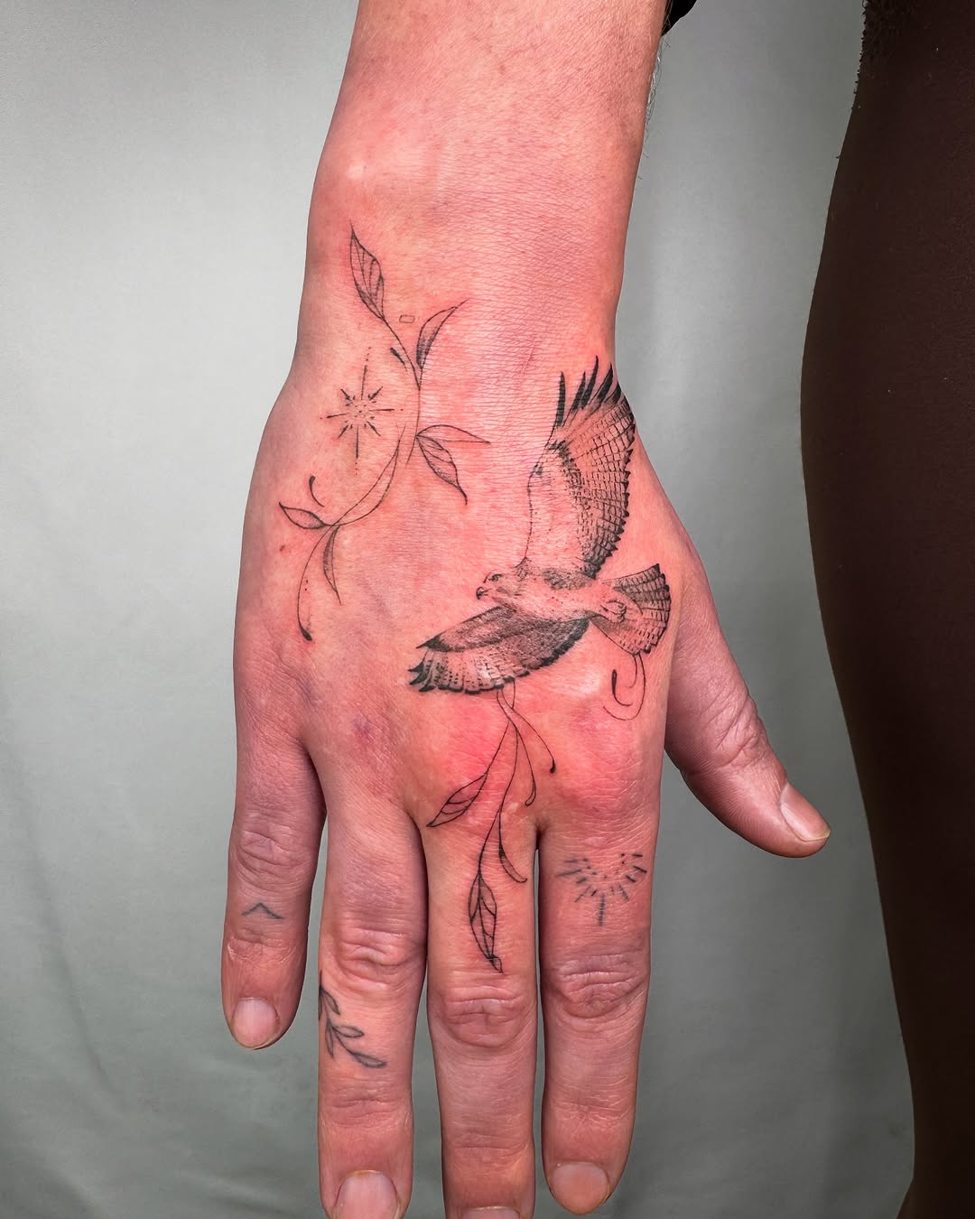 Elegant hawk tattoo with floral elements on hand