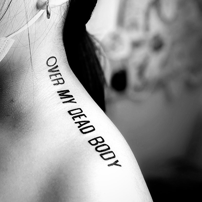 Bold quote tattoo on exposed shoulder