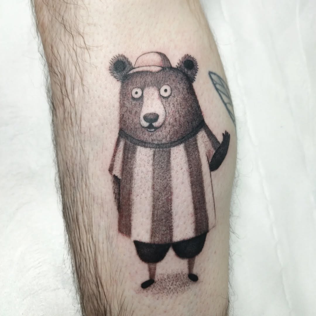Playful cartoon bear tattoo with striped shirt