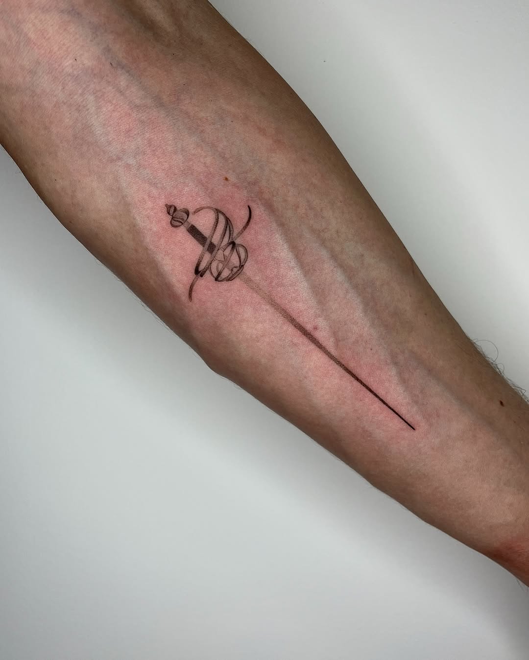 Elegant minimalist sword tattoo on forearm